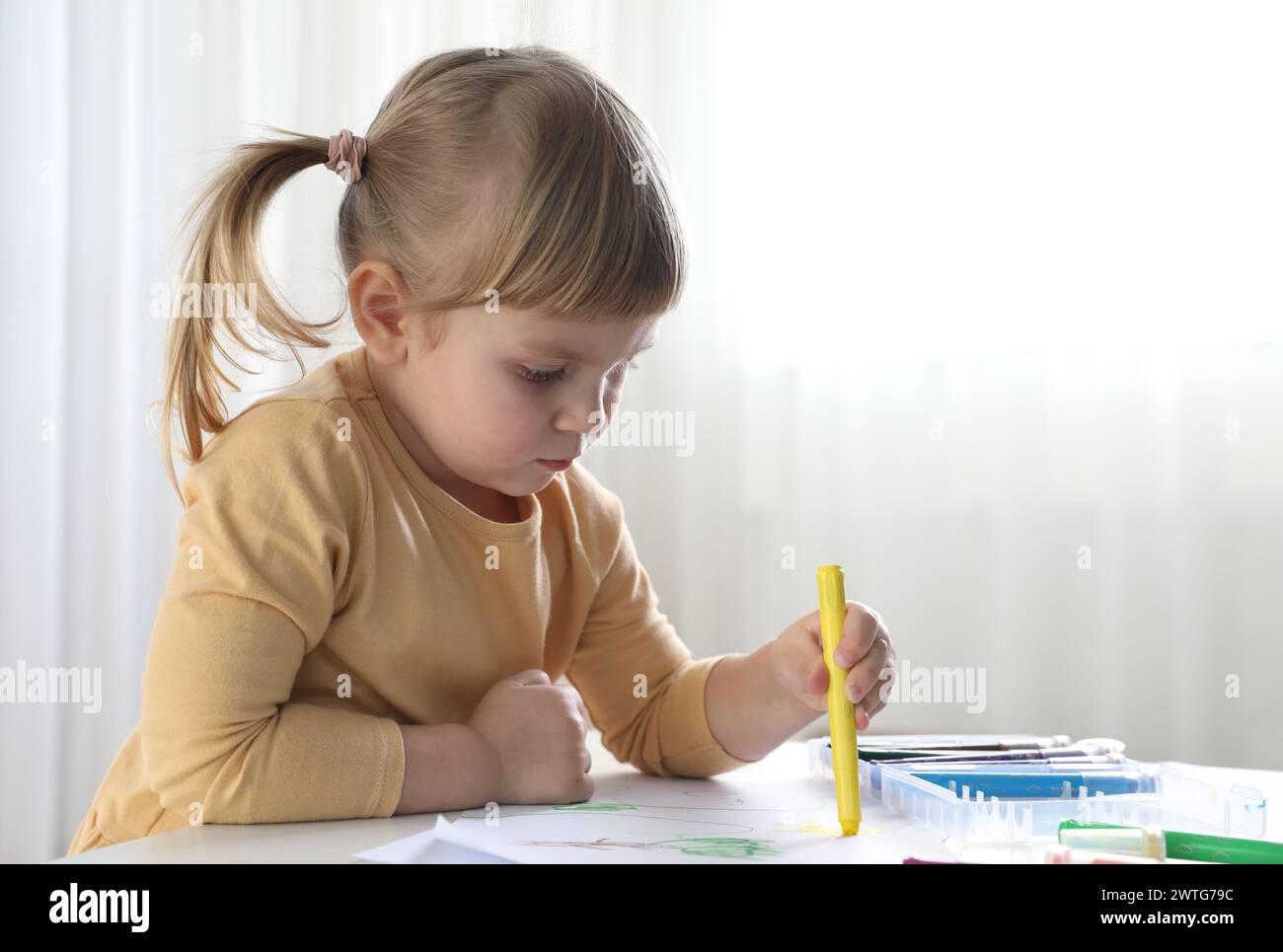 Cute little girl drawing with marker at white table indoors. Child`s art Stock Photo